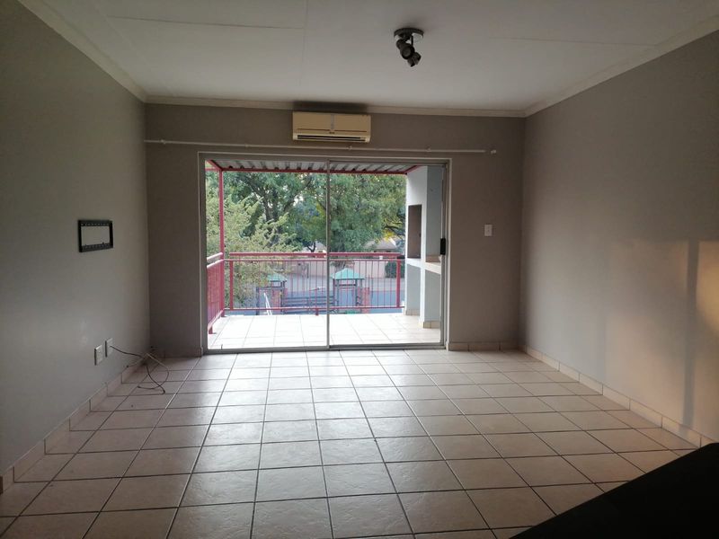 An empty living room featuring ceramic floor tiles, a wall-mounted air conditioner, and sliding glass doors leading to an outdoor balcony area.