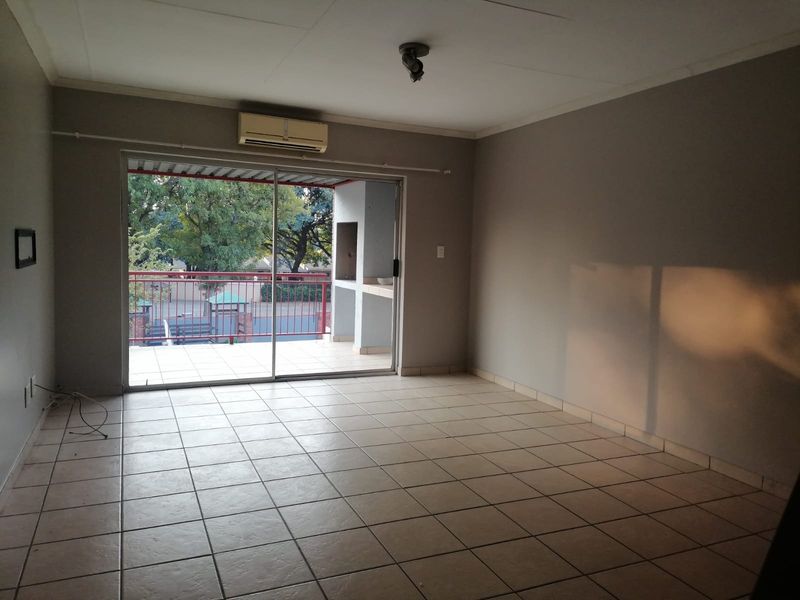 An empty living room featuring tiled flooring, a wall-mounted air conditioning unit, and a sliding glass door leading to a balcony with a built-in braai.
