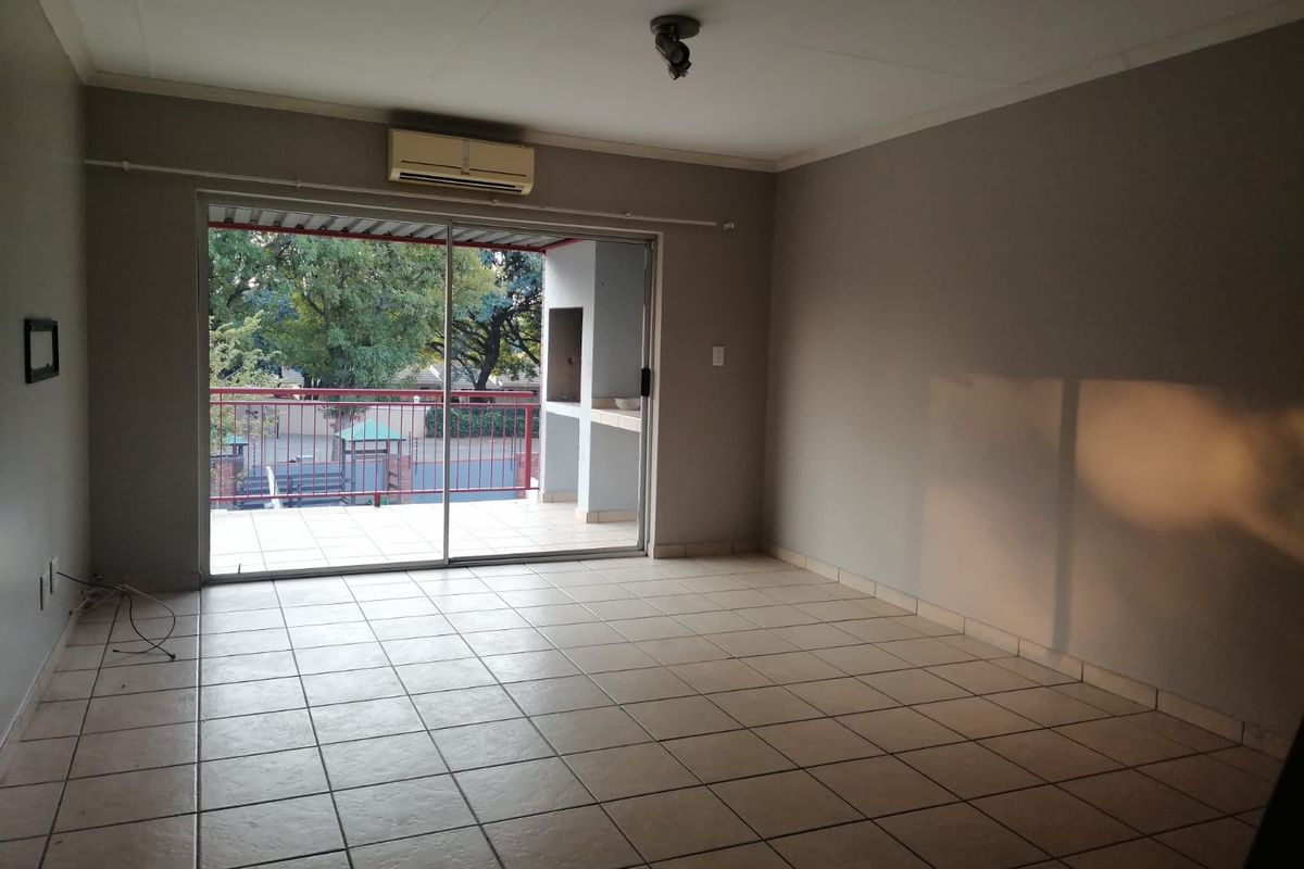 An empty living room featuring tiled flooring, a wall-mounted air conditioning unit, and a sliding glass door leading to a balcony with a built-in braai.