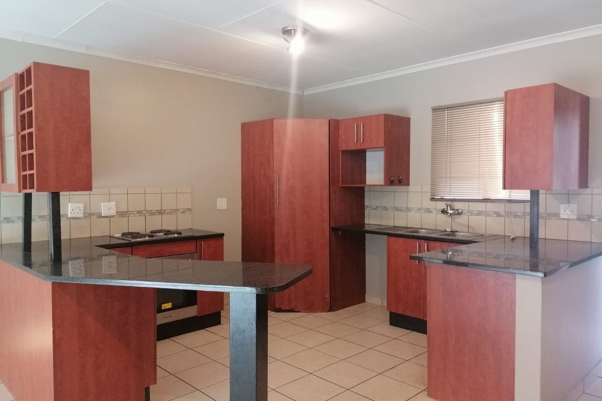 A functional kitchen featuring dark wood cabinetry, granite countertops, a built-in oven, electric hob, and a double sink with tiled backsplash.