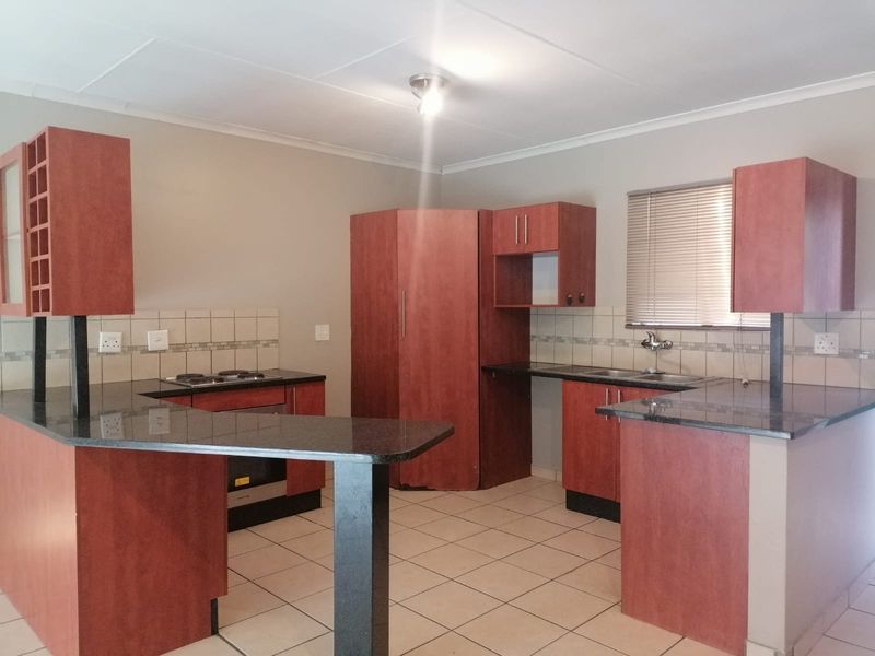A functional kitchen featuring dark wood cabinetry, granite countertops, a built-in oven, electric hob, and a double sink with tiled backsplash.