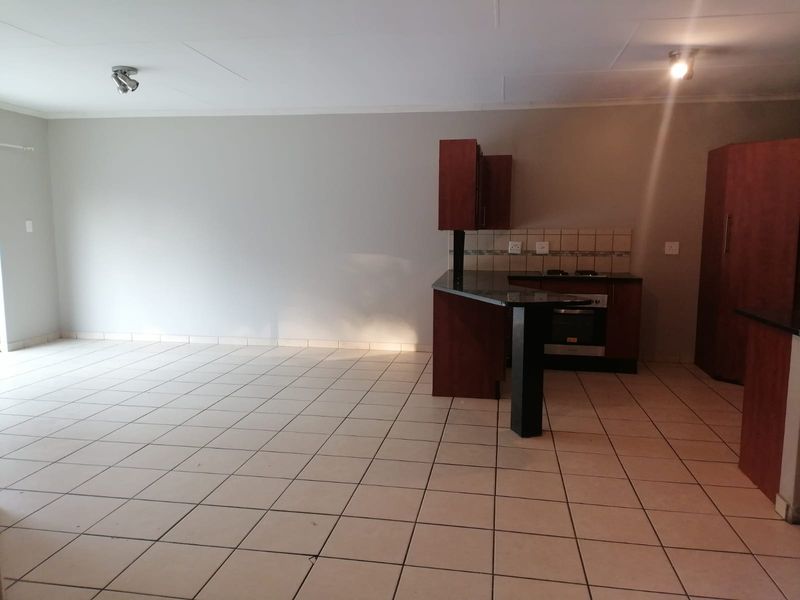 An open-plan living and kitchen area featuring tiled flooring, dark wood cabinetry, granite countertops, and built-in cooking appliances.