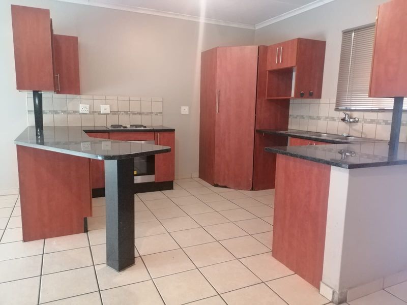 A functional kitchen featuring built-in wooden cabinetry, granite countertops, a tiled backsplash, and integrated oven and hob, set on ceramic tiled flooring.
