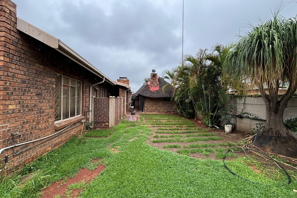 Rear exterior view of a face brick townhouse featuring a thatched roof structure, a small garden area, and perimeter boundary walls.