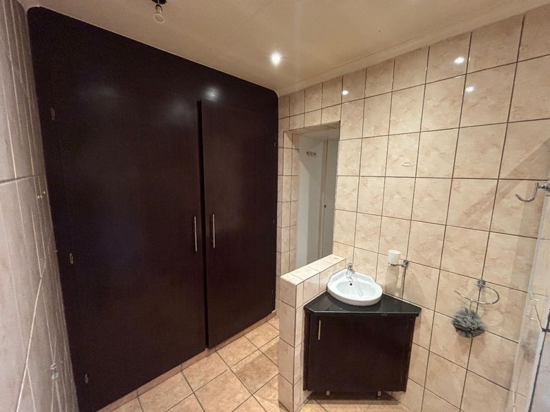A functional bathroom featuring a corner vanity unit, built-in storage cupboards, and tiled finishes throughout.