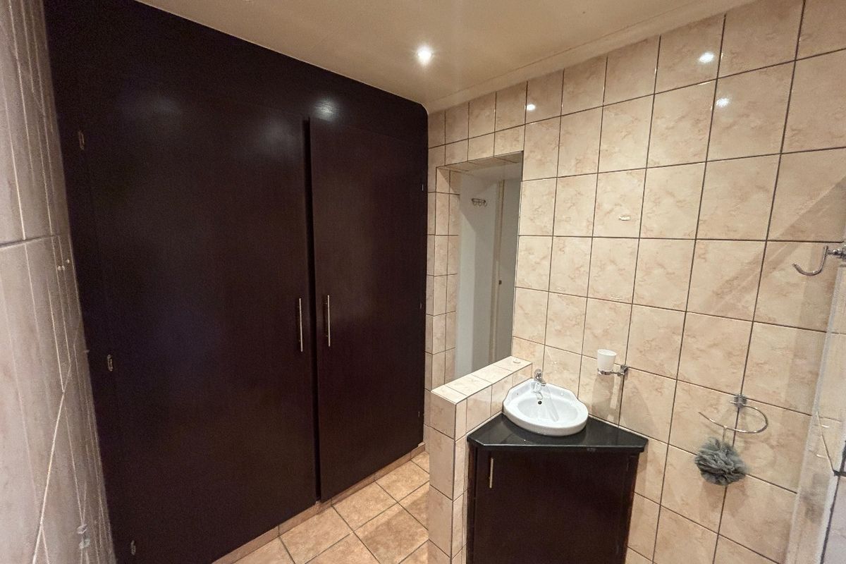 A functional bathroom featuring a corner vanity unit, built-in storage cupboards, and tiled finishes throughout.