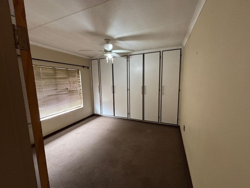 A spacious, empty bedroom featuring built-in cupboards, a ceiling fan, and venetian blinds, offering a neutral canvas for personalization.