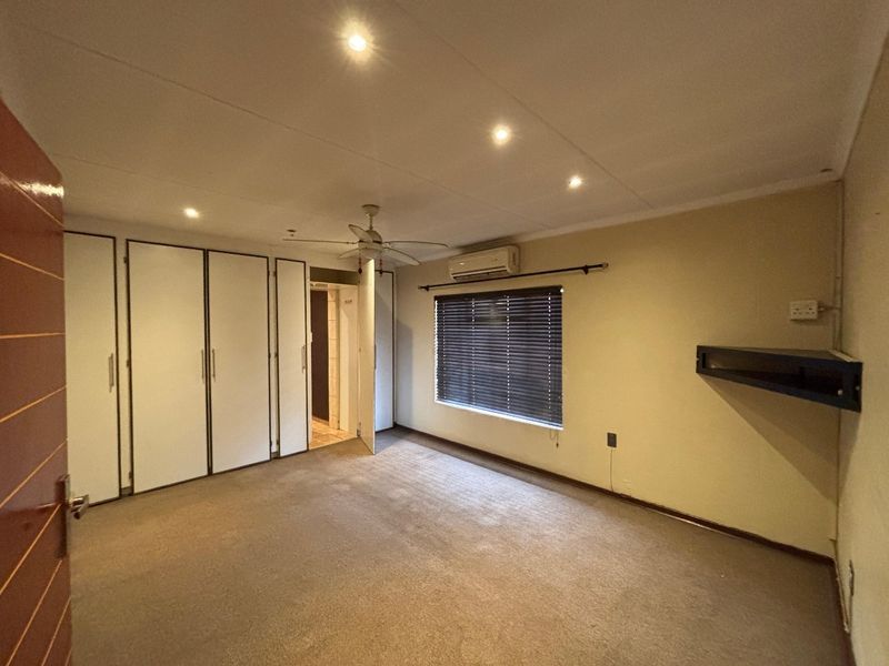 Spacious bedroom featuring built-in cupboards, air conditioning, ceiling fan, and neutral carpeting, offering a blank canvas for personalization.
