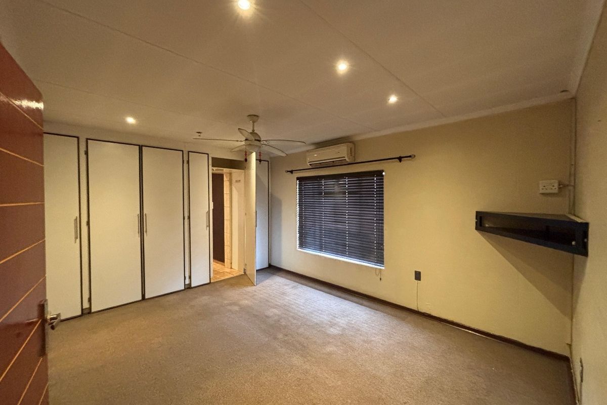 Spacious bedroom featuring built-in cupboards, air conditioning, ceiling fan, and neutral carpeting, offering a blank canvas for personalization.