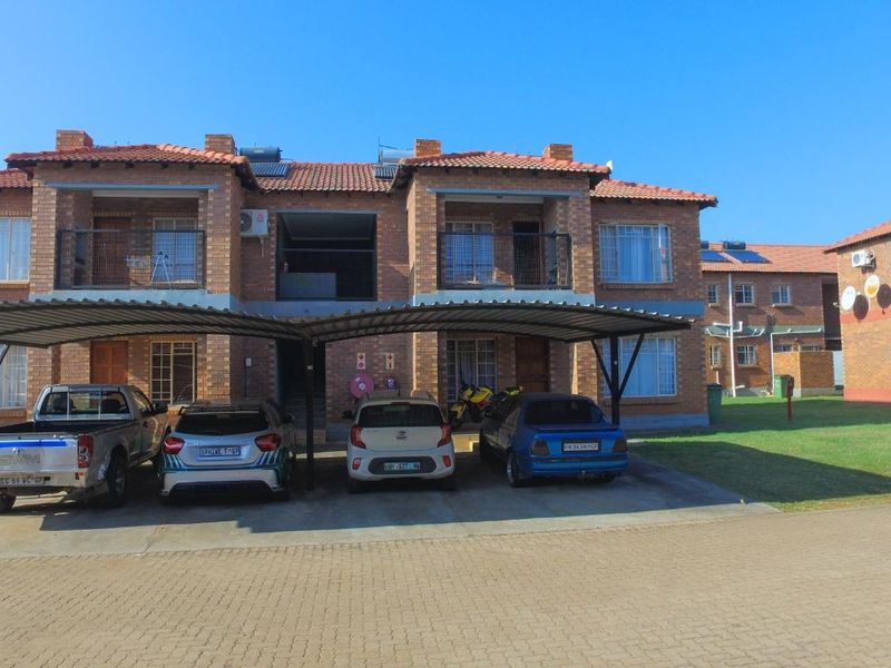 Front view of a face brick apartment complex featuring covered parking bays, tiled roofing, and private balconies.