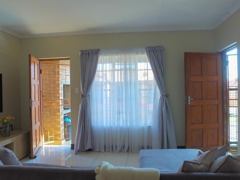 A living room featuring tiled flooring, wooden panel doors, and access to an outdoor area with a built-in braai.