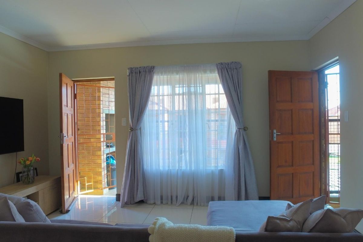 A living room featuring tiled flooring, wooden panel doors, and access to an outdoor area with a built-in braai.