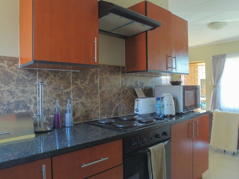 A functional kitchen featuring wood-finish cabinetry, granite countertops, a marble-effect tiled backsplash, and integrated electric cooking appliances.