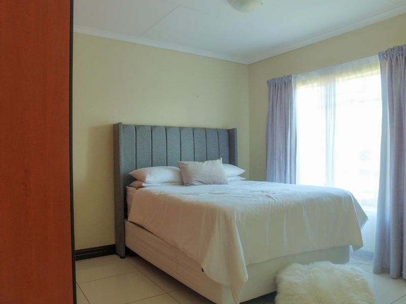 A functional bedroom featuring tiled flooring, a built-in wardrobe, and large windows with curtain rails, providing natural light.