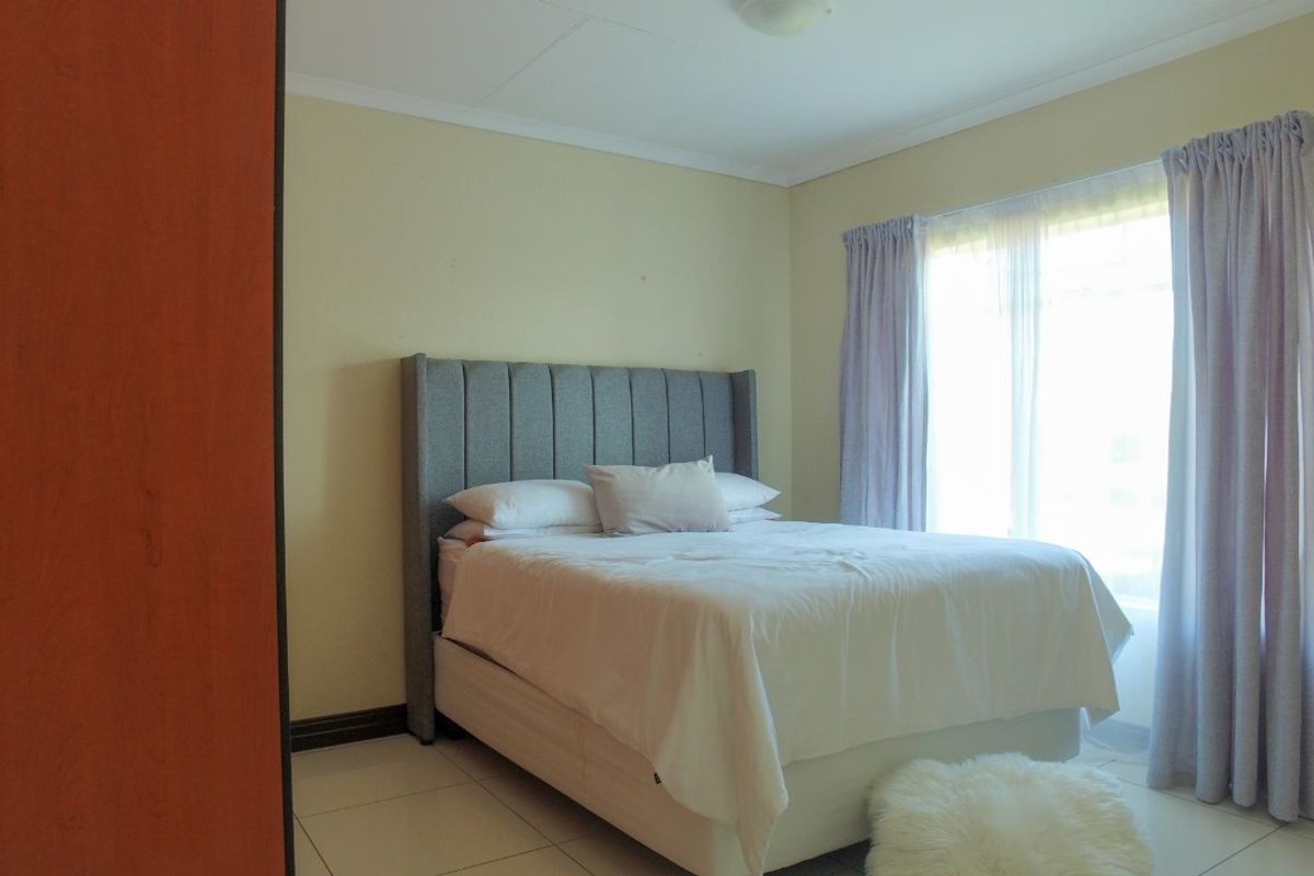 A functional bedroom featuring tiled flooring, a built-in wardrobe, and large windows with curtain rails, providing natural light.