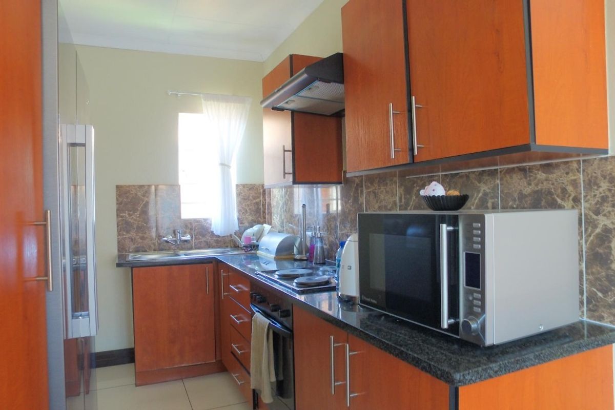 A functional kitchen featuring wood-finish cabinetry, granite countertops, a built-in oven with hob, and a tiled splashback.