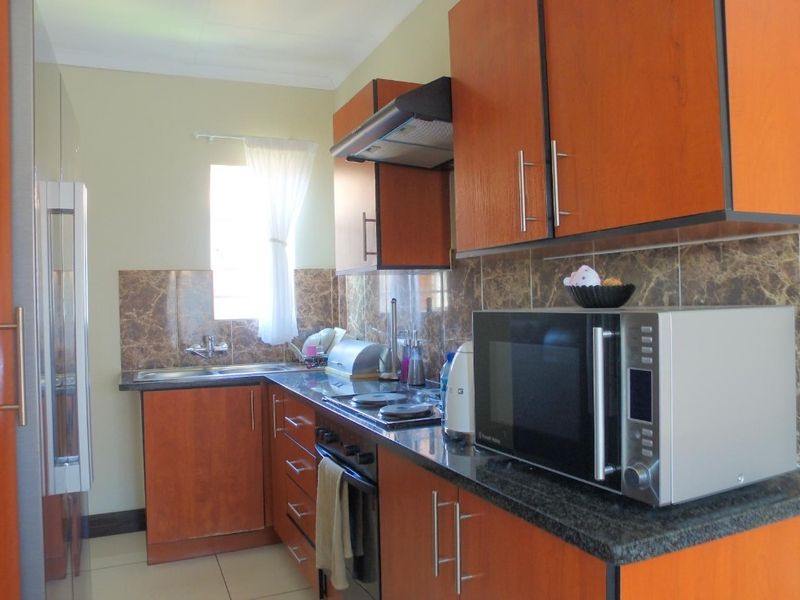 A functional kitchen featuring wood-finish cabinetry, granite countertops, a built-in oven with hob, and a tiled splashback.