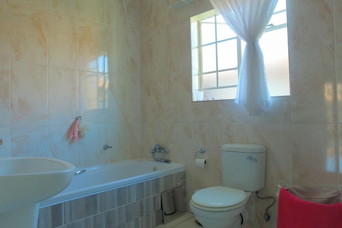 A functional bathroom featuring a pedestal basin, bathtub, and toilet with neutral wall tiling and natural light from a window.