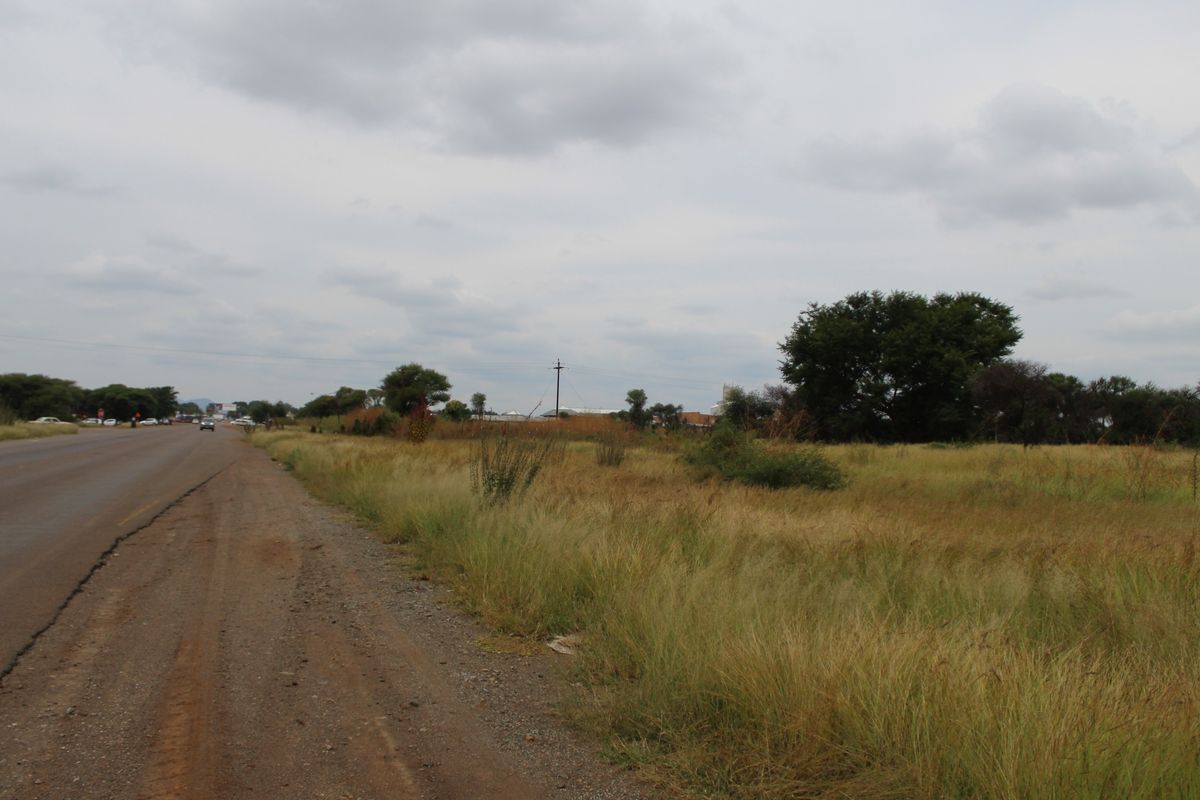 A view of the vacant residential land parcel adjacent to the main road, featuring natural grass coverage and established trees.