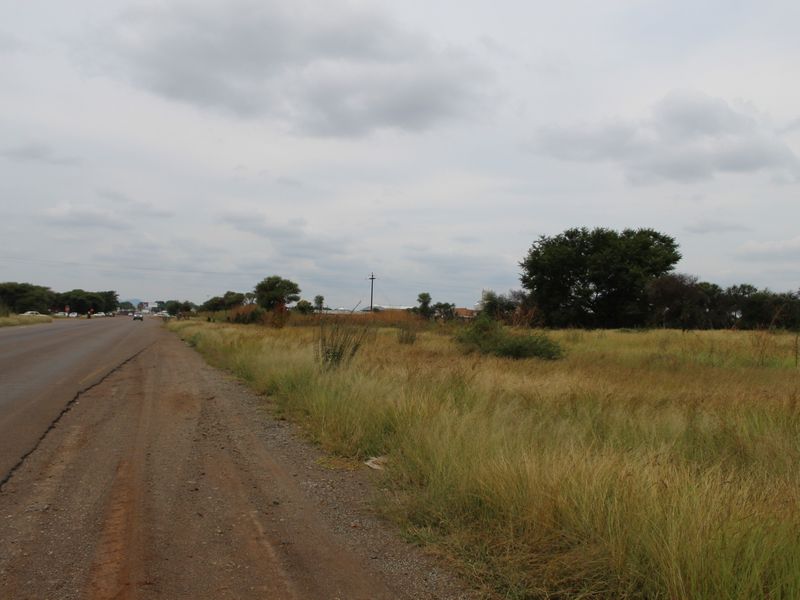 A view of the vacant residential land parcel adjacent to the main road, featuring natural grass coverage and established trees.