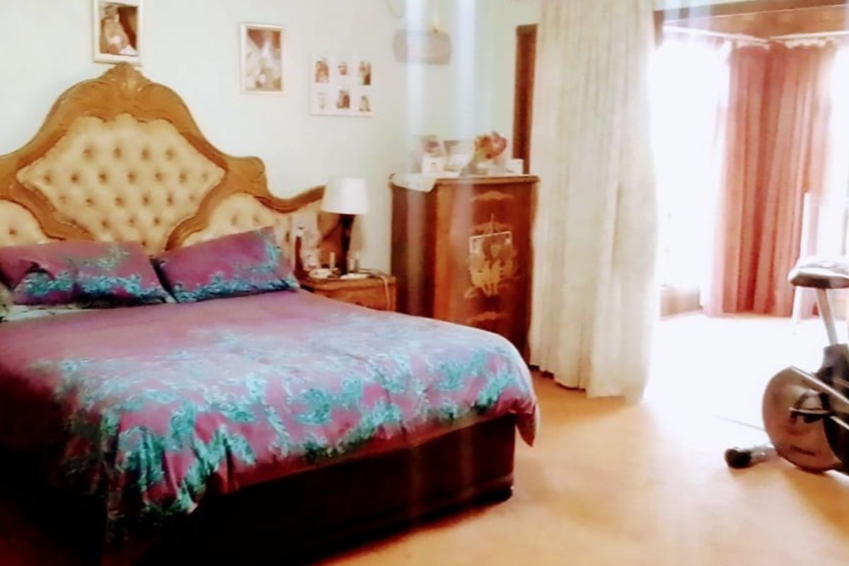 A spacious bedroom featuring neutral walls, tiled flooring, and direct access to an adjoining area through a large doorway with curtains.