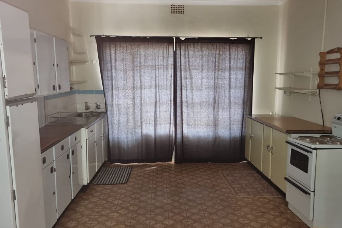 A dated kitchen featuring original cabinetry, laminate countertops, a freestanding stove, and vinyl flooring, offering significant potential for a modern renovation.