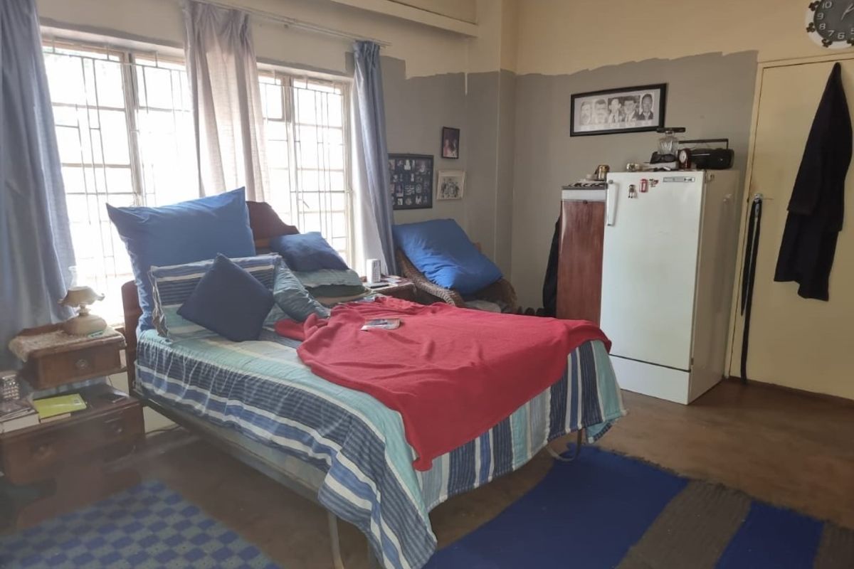 A bedroom featuring large windows with security bars, neutral wall tones, and basic flooring, offering a functional space with potential for cosmetic updates.