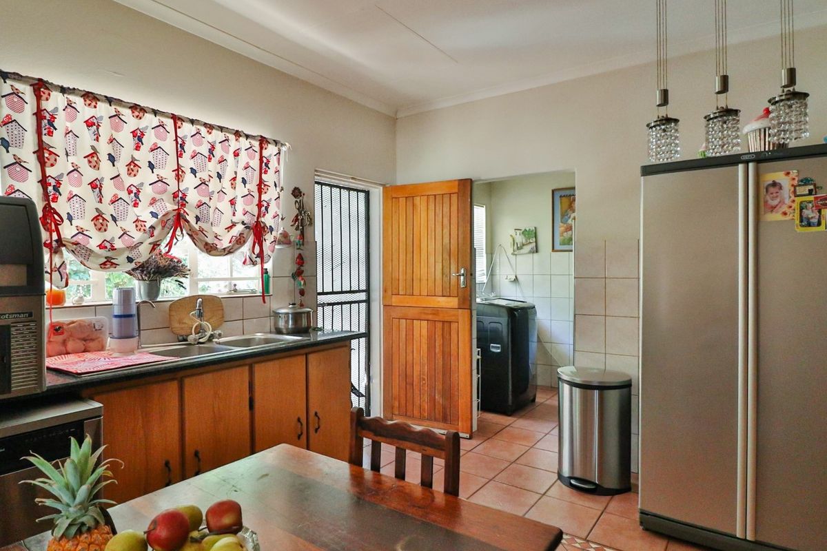 Kitchen featuring wooden cabinetry, tiled flooring, and a double sink, with an adjacent scullery area visible through the doorway.