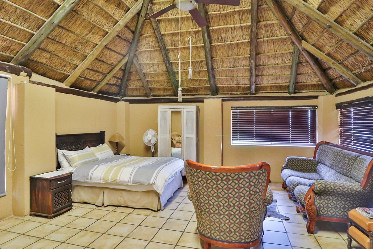 Spacious bedroom featuring a traditional thatched roof with exposed timber beams, tiled flooring, and large windows with fitted blinds.