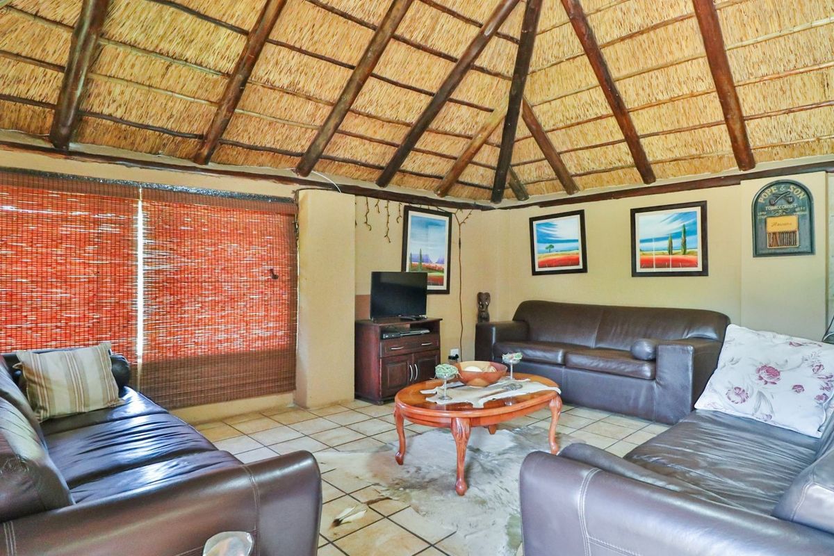 A rustic living room featuring a high vaulted thatched roof with exposed timber beams and tiled flooring.