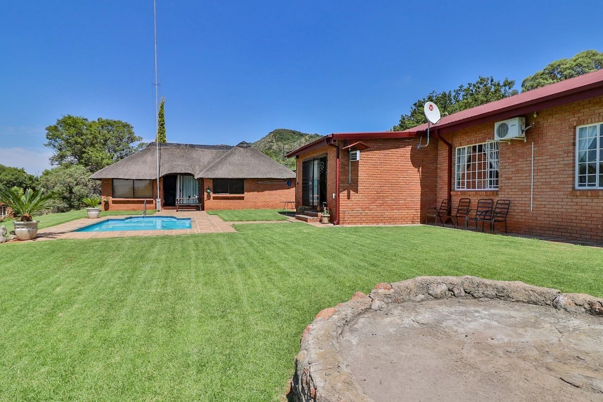 Spacious rear garden featuring a swimming pool, a thatched-roof outbuilding, and a stone fire pit, set against a scenic rural landscape.