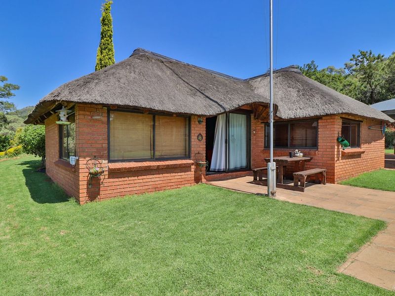 A charming brick farmhouse featuring a traditional thatched roof, a paved patio area, and well-maintained surrounding lawns.