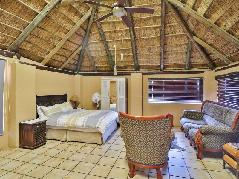 Spacious bedroom featuring a traditional thatched roof with exposed timber beams, tiled flooring, and large windows with fitted blinds.