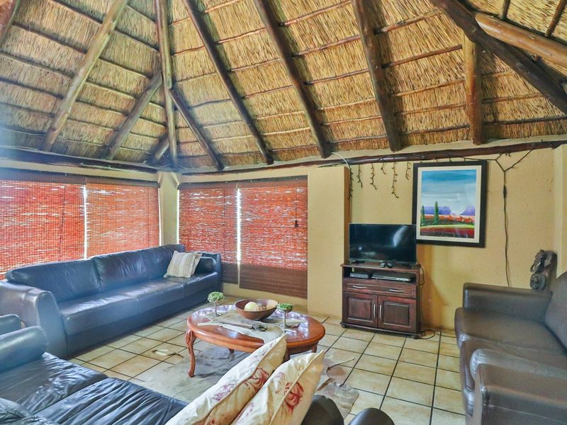 A rustic living room featuring a high vaulted thatched roof with exposed timber beams and tiled flooring.