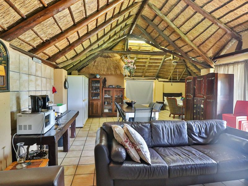 Spacious open-plan living area featuring a high vaulted thatch roof with exposed timber beams and tiled flooring.