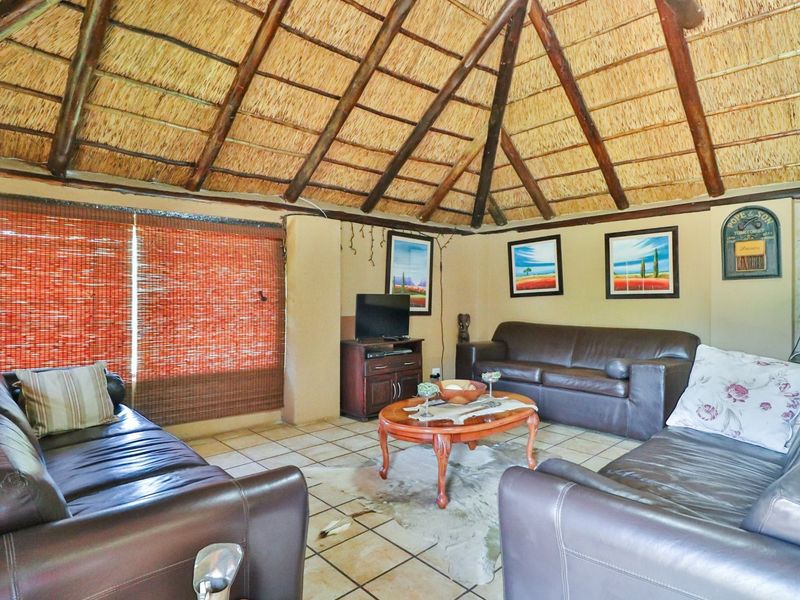 A rustic living room featuring a high vaulted thatched roof with exposed timber beams and tiled flooring.