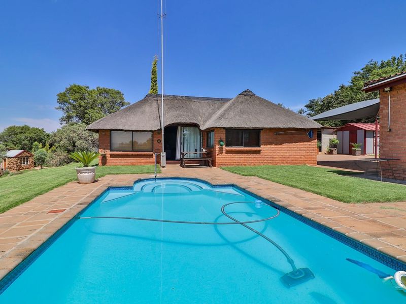 A well-maintained farm property featuring a thatched-roof brick dwelling, a paved pool deck, and a swimming pool set within a landscaped garden.