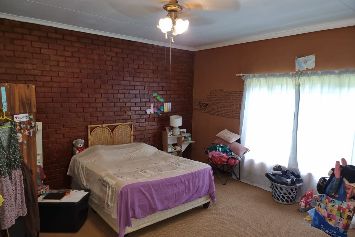 Spacious bedroom featuring a rustic exposed brick feature wall, ceiling fan, and large window allowing for natural light.
