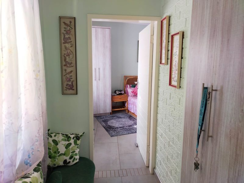 A hallway featuring a textured brick wall and built-in cupboards, providing access to an adjacent bedroom with tiled flooring throughout.