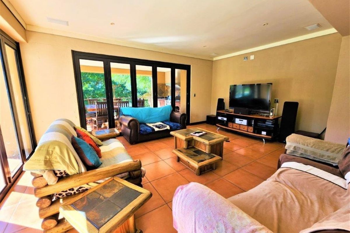 Spacious living room featuring large black-framed folding glass doors that open onto an outdoor patio area, with terracotta floor tiles throughout.