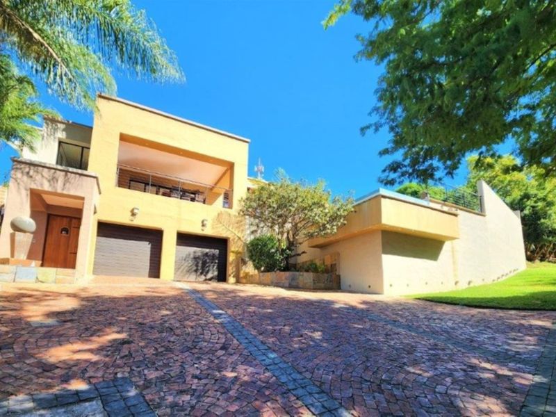 Front elevation of a multi-level house featuring a double garage, paved driveway, and an upper-level balcony.