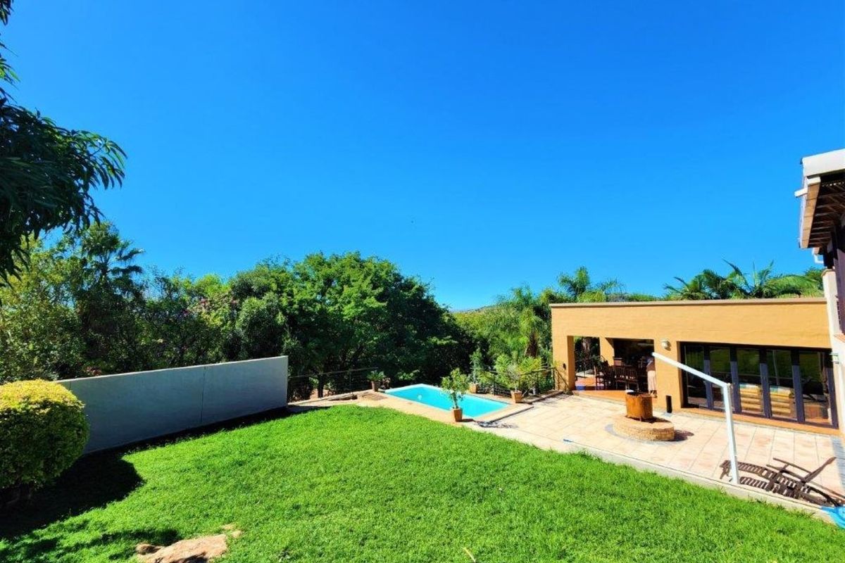 Rear exterior view featuring a well-maintained lawn, a swimming pool, and a spacious tiled patio area connected to the main house.