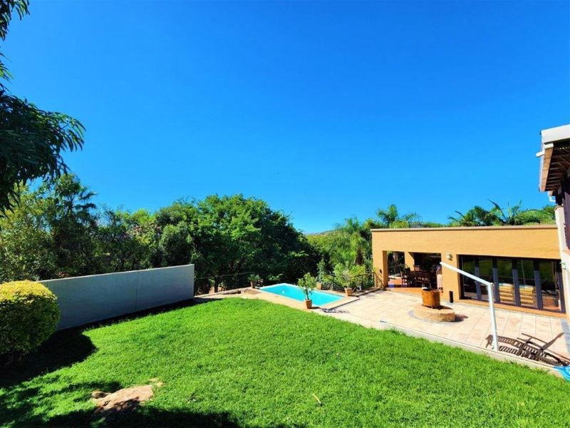 Rear exterior view featuring a well-maintained lawn, a swimming pool, and a spacious tiled patio area connected to the main house.