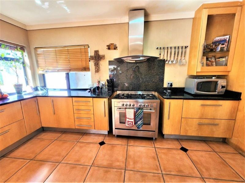 A functional kitchen featuring wooden cabinetry, granite countertops, a stainless steel gas stove with extractor fan, and tiled flooring.