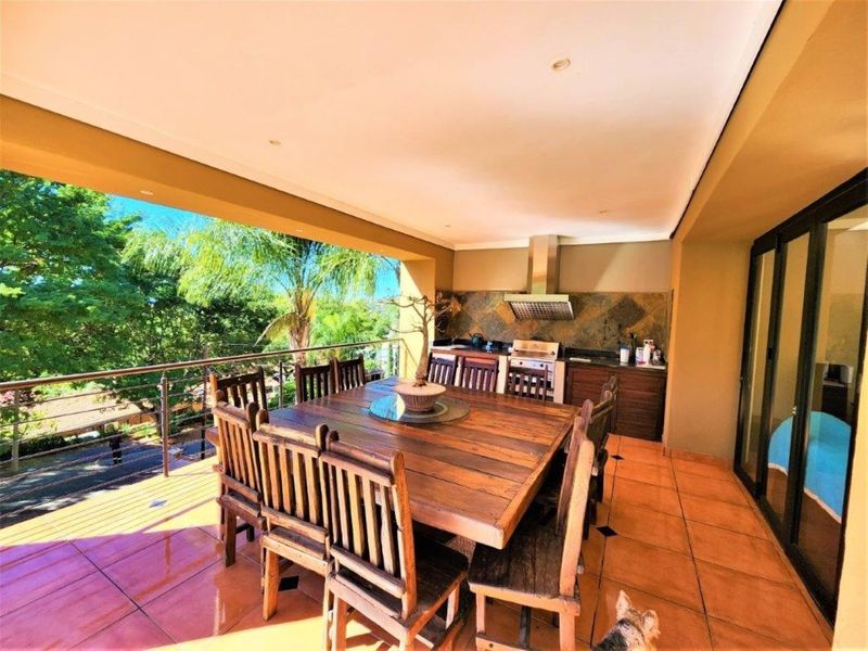 Spacious covered patio featuring a built-in braai area, tiled flooring, and stainless steel balustrades, perfect for outdoor entertaining.