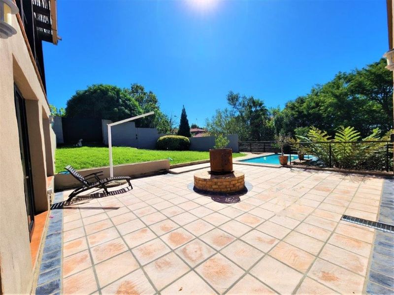 Spacious rear patio area featuring tiled flooring, a central brick planter, and an adjacent swimming pool set within a landscaped garden.