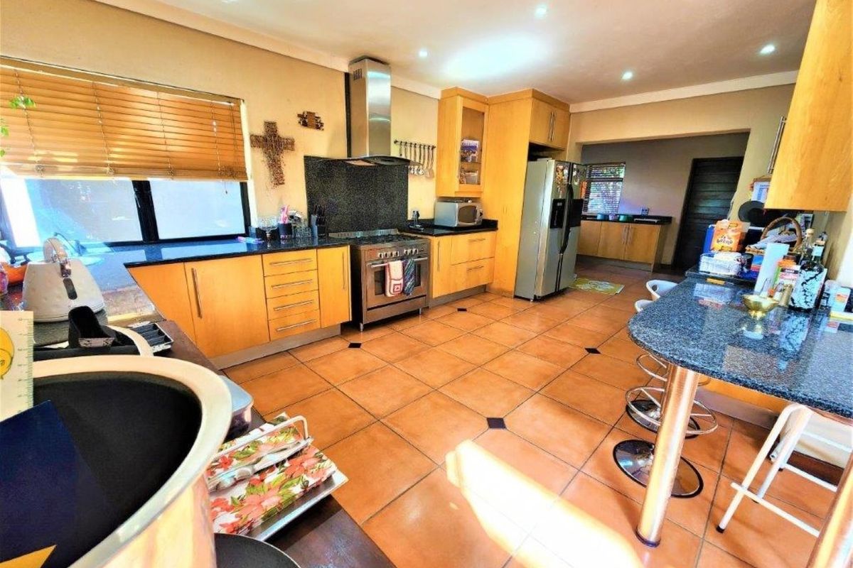 Spacious kitchen featuring wooden cabinetry, granite countertops, a breakfast bar, and a stainless steel gas stove with an extractor fan.