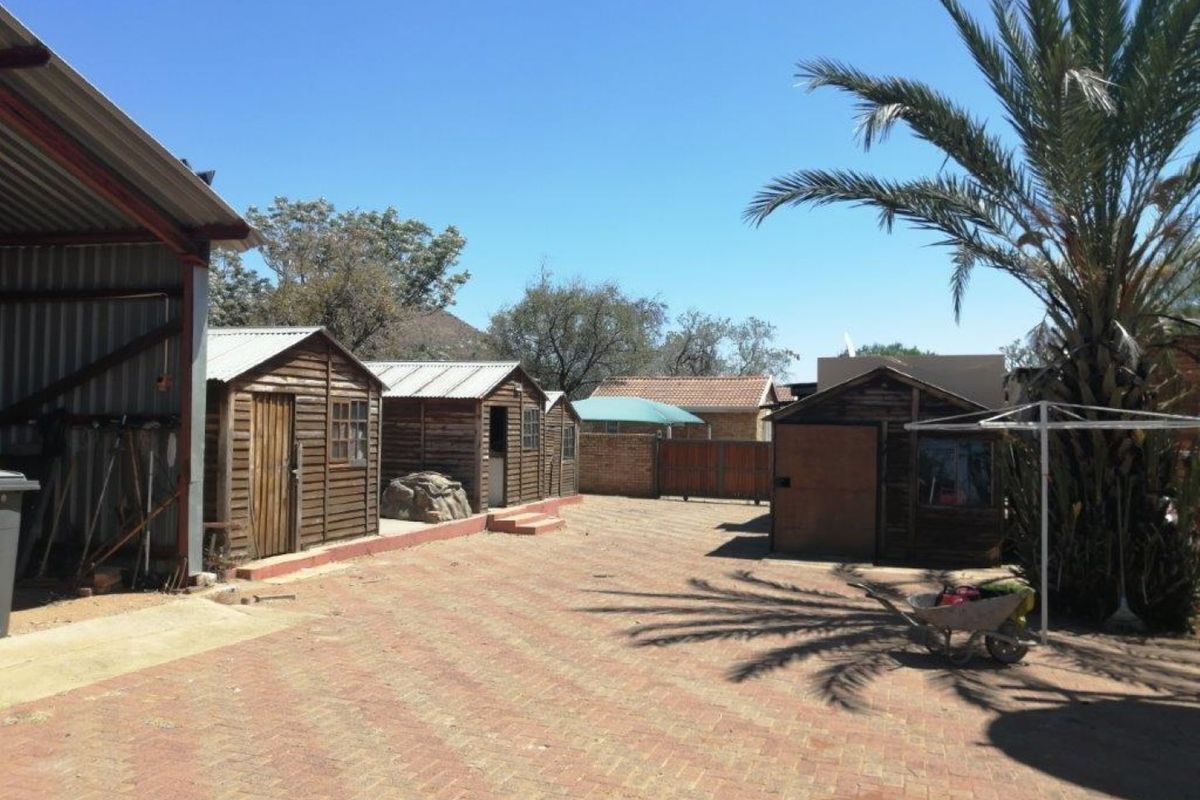 A farm yard area featuring multiple timber outbuildings, a large metal-roofed structure, and paved ground surfaces.