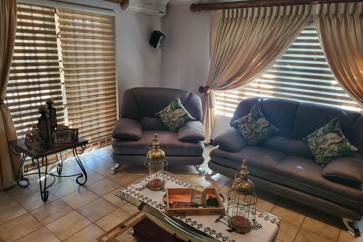 A comfortable living room featuring tiled flooring, wall-mounted air conditioning unit, and large windows with fitted blinds and curtain rods.