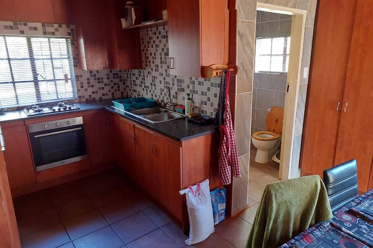 A functional kitchen featuring wooden cabinetry, a built-in oven and hob, and a tiled backsplash, with an adjacent bathroom access.